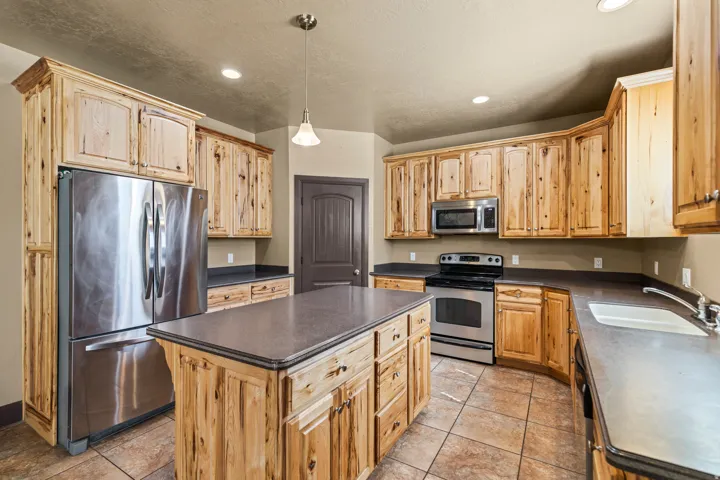 Kitchen with stainless steel appliances, dark countertops, a kitchen island, decorative light fixtures, and light wood finish cabinetry
