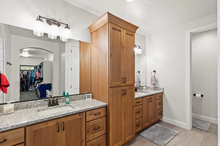 Bathroom featuring a spacious closet, two vanities, and light wood-style floors