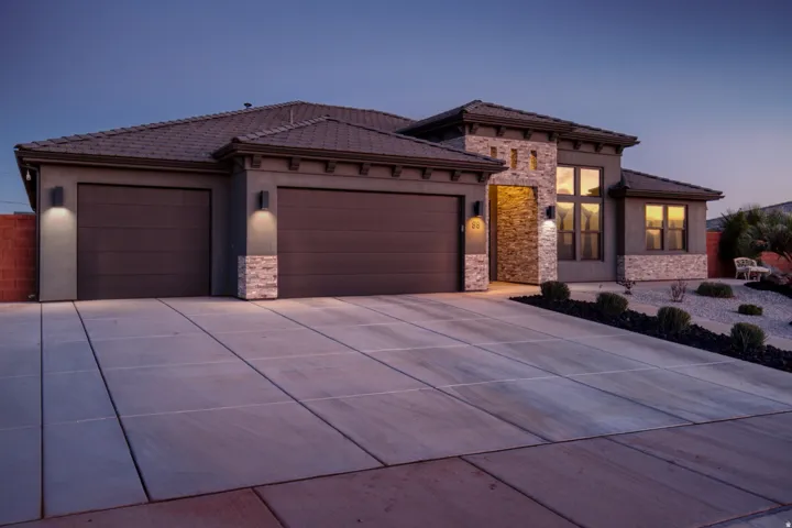 View of front of home with stone siding, an attached garage, driveway, and stucco siding