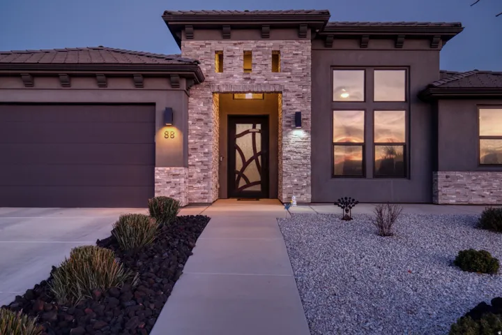 View of front of property with a garage, a tiled roof, stucco siding, and stone siding