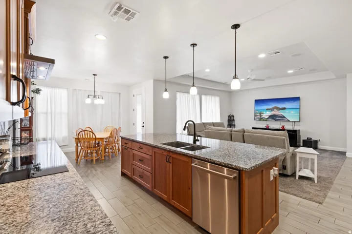 Kitchen with light stone counters, wood finish cabinets, a kitchen island with sink, dishwasher, and wood finish floors