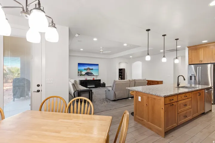 Kitchen featuring hanging light fixtures, open floor plan, a center island with sink, light stone countertops, and arched walkways