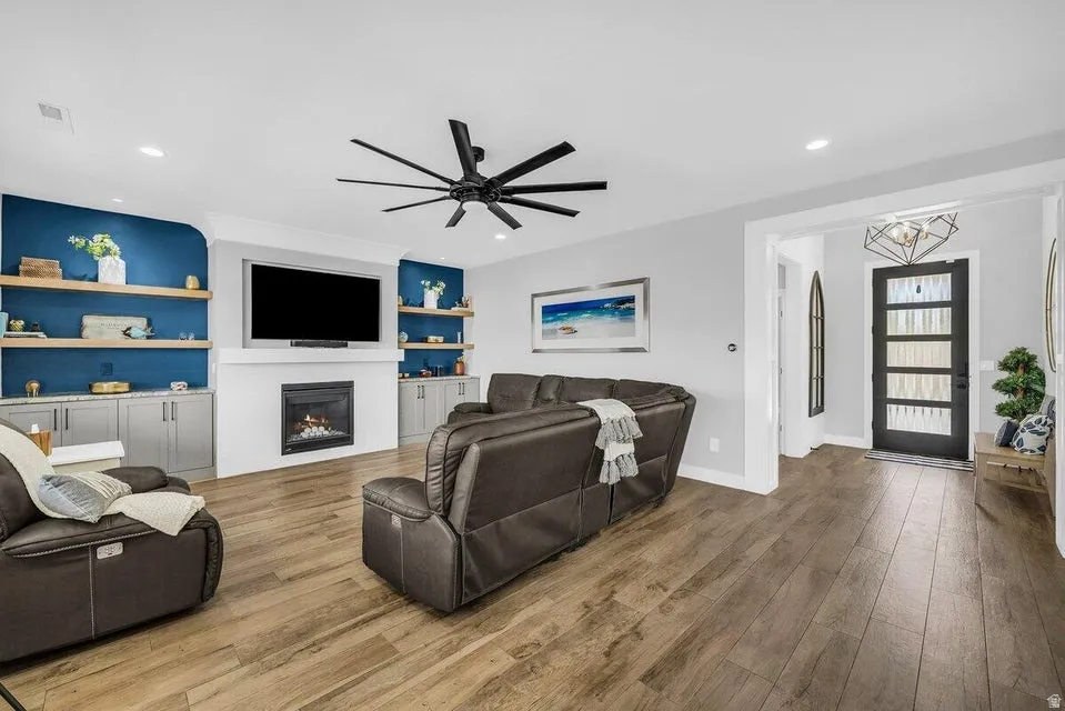 Living room featuring built in shelves, a ceiling fan, wood finished floors, and a glass covered fireplace