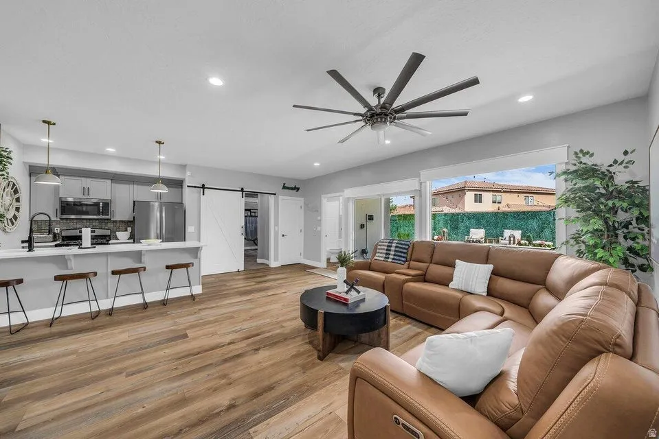 Living room featuring a barn door, light wood-style flooring, a ceiling fan, and recessed lighting