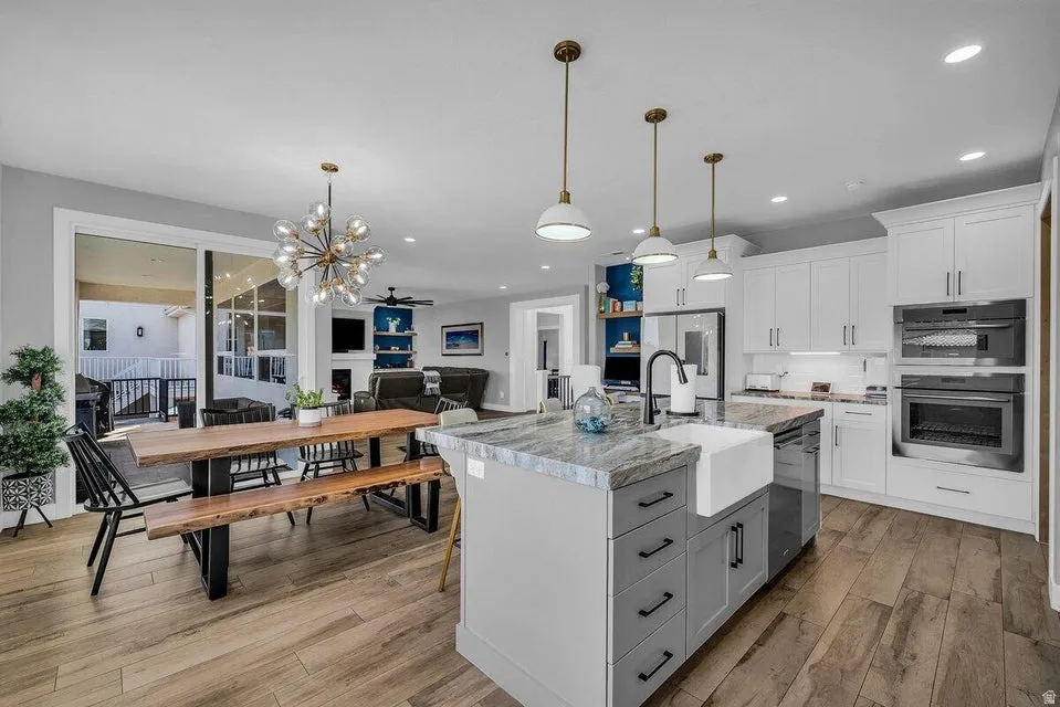 Two tone kitchen with a center island with sink, a chandelier, ceiling fan, light wood-style floors, and decorative backsplash