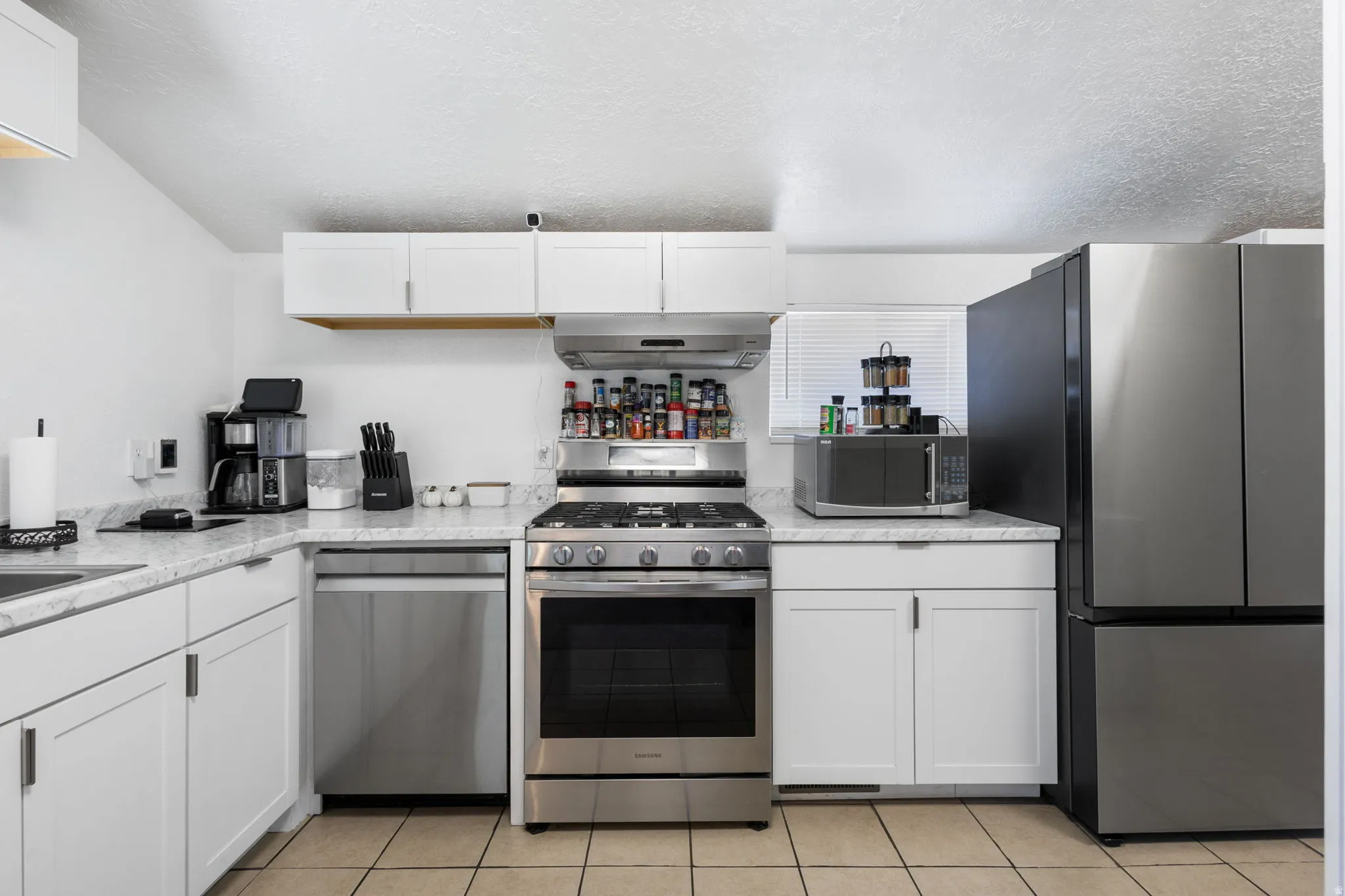 Kitchen with stainless steel appliances, white cabinets, a textured ceiling, and light tile patterned floors