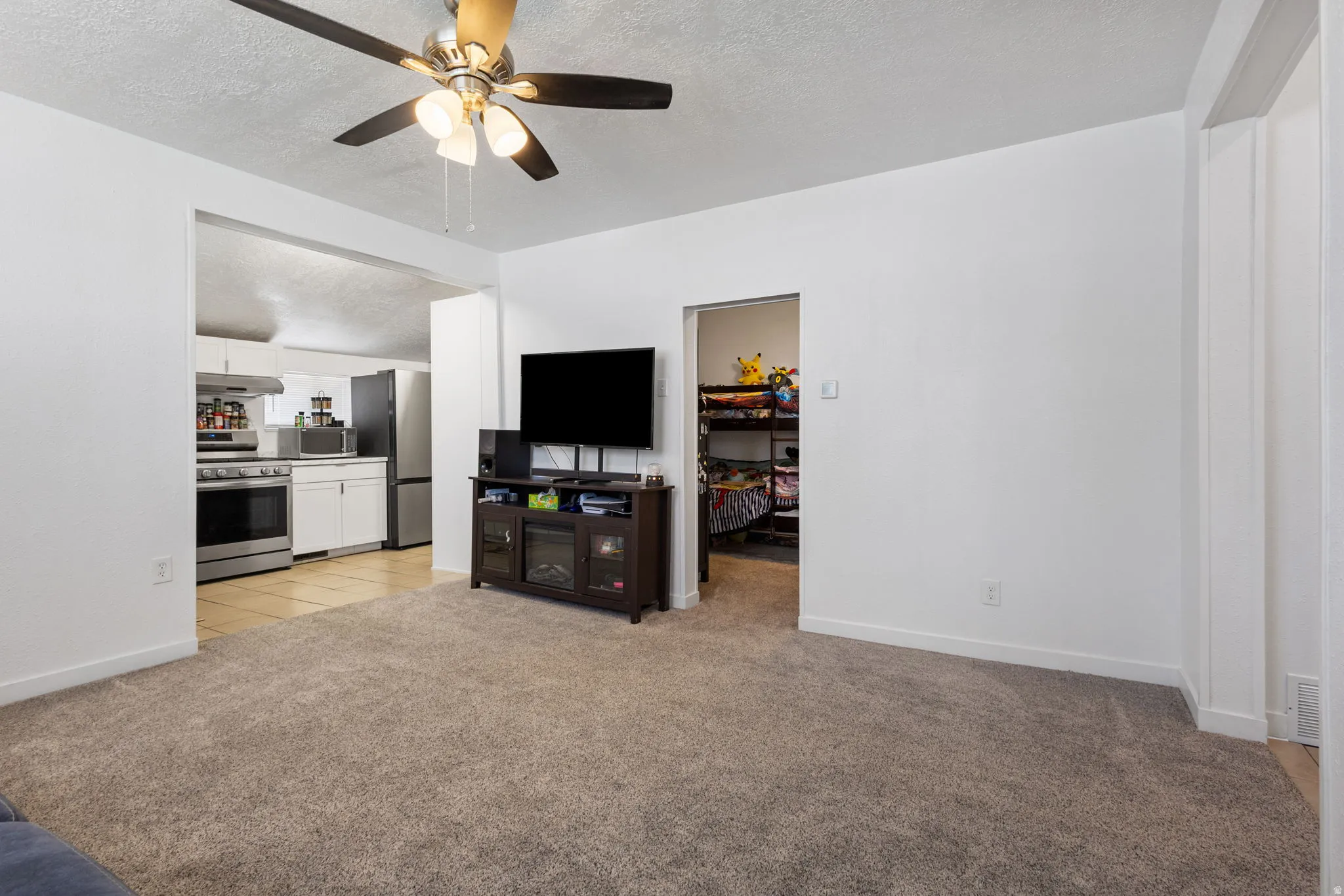 Living area with a textured ceiling, light carpet, and ceiling fan