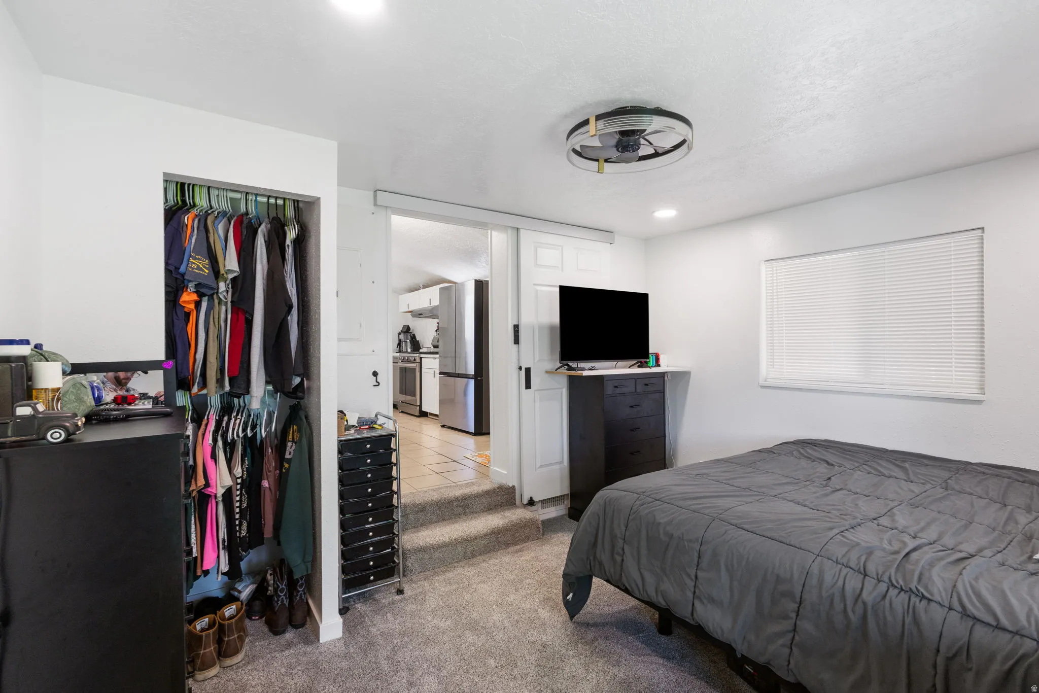 Bedroom with a closet, freestanding refrigerator, light colored carpet, and recessed lighting