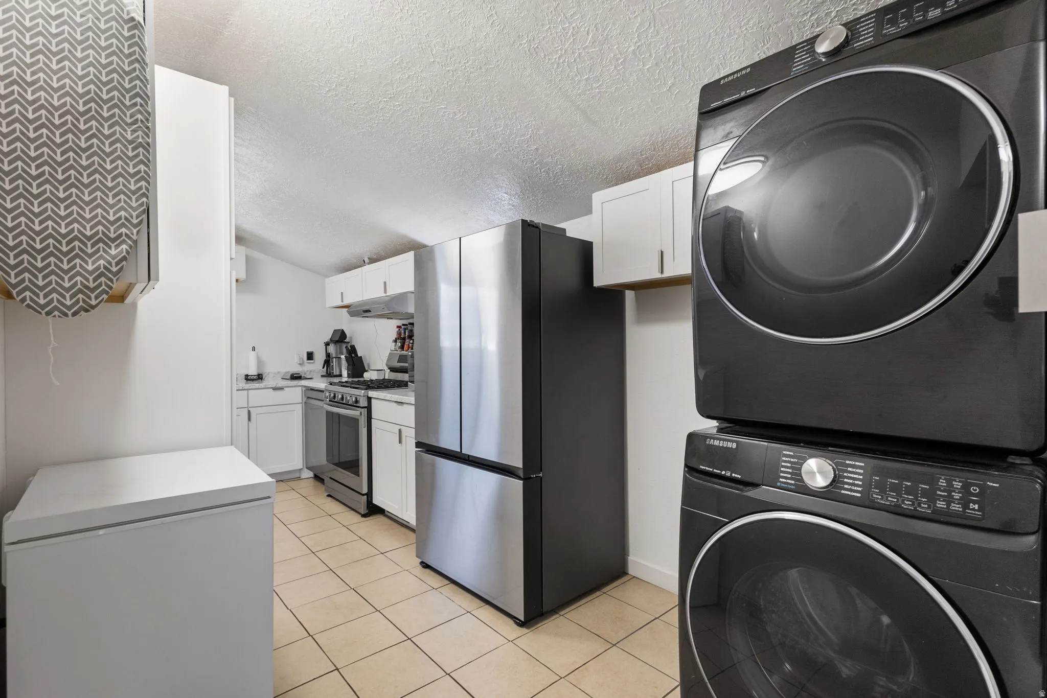 Laundry area with stacked washer / dryer, a textured ceiling, and light tile patterned floors