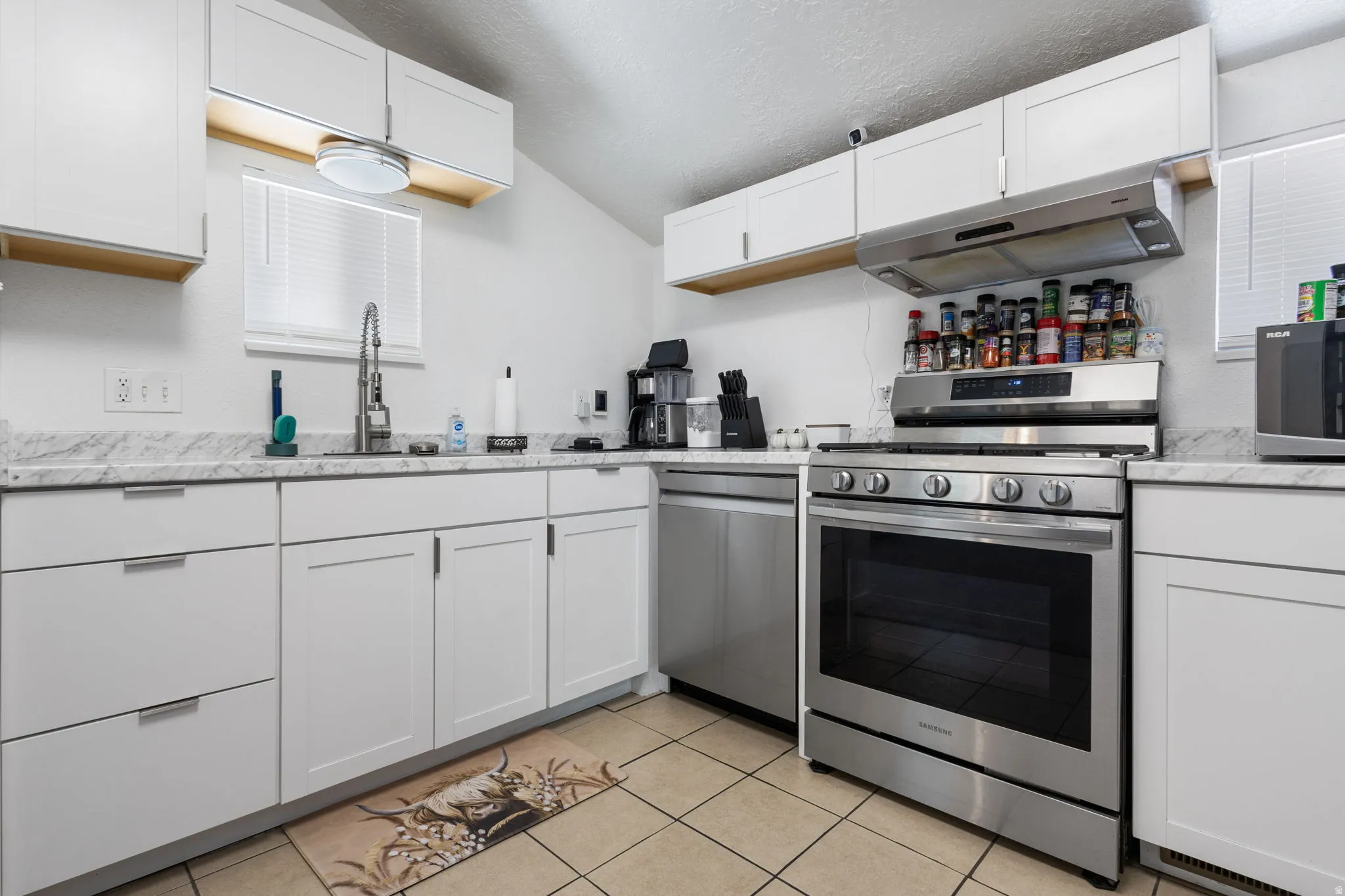 Kitchen with white cabinetry, stainless steel appliances, light tile patterned floors, a textured ceiling, and light stone countertops