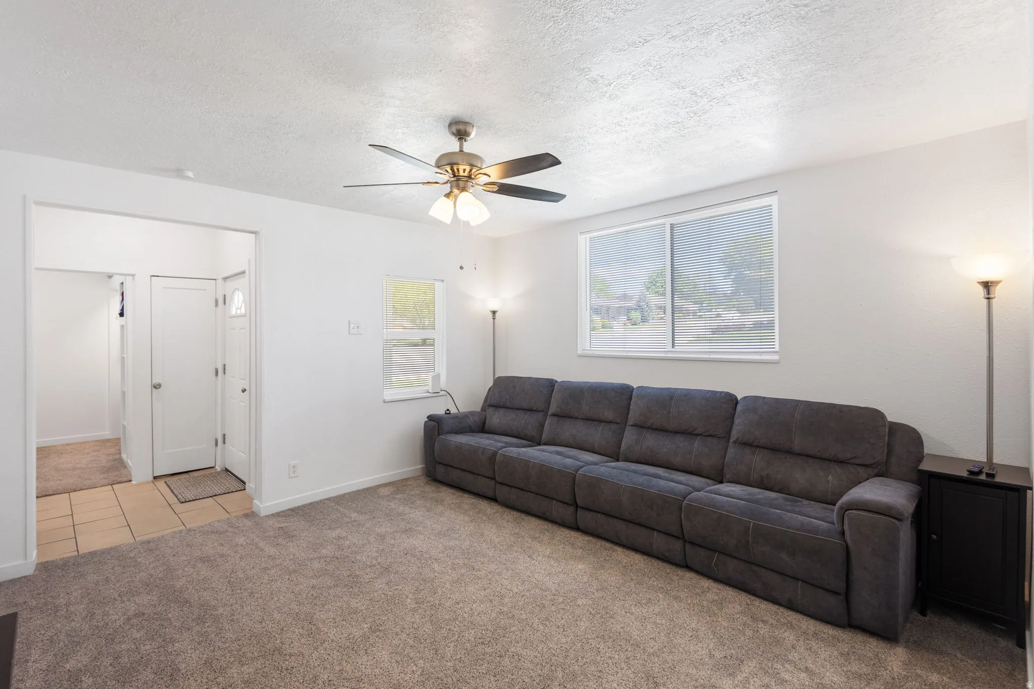Living area featuring light colored carpet, a textured ceiling, and ceiling fan