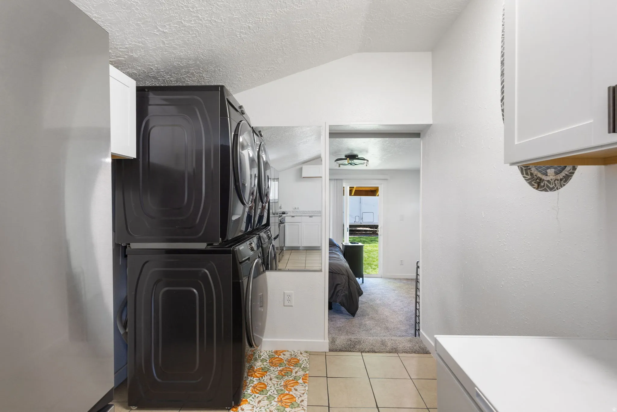 Laundry area with light colored carpet, stacked washer and clothes dryer, cabinet space, light tile patterned floors, and a textured wall