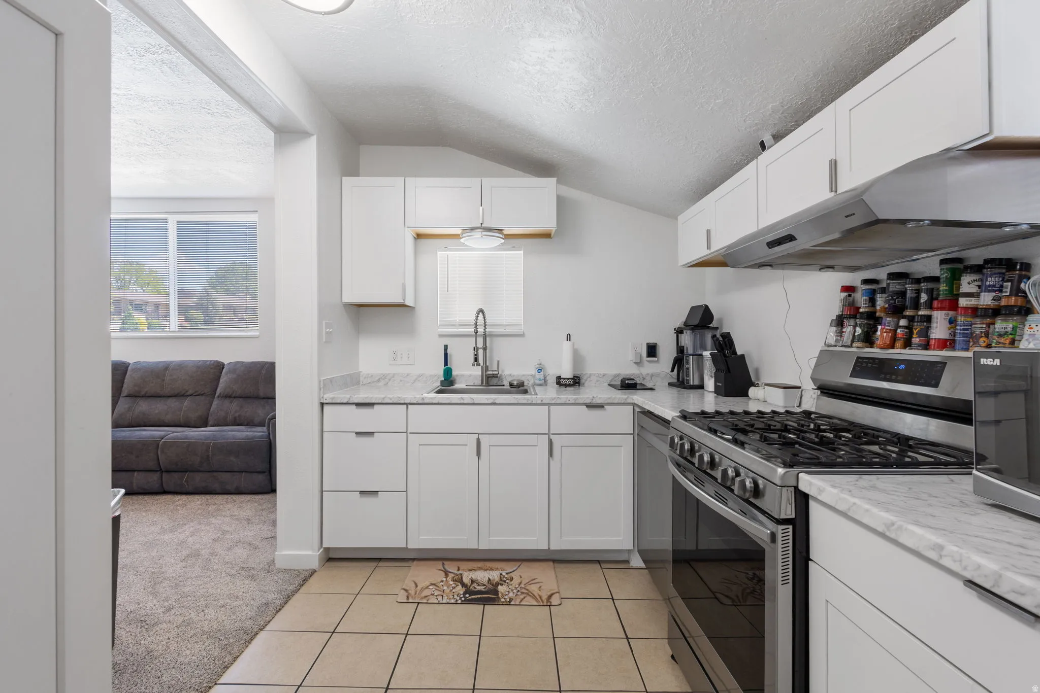 Kitchen featuring stainless steel range with gas cooktop, white cabinets, light colored carpet, light tile patterned flooring, and light stone counters