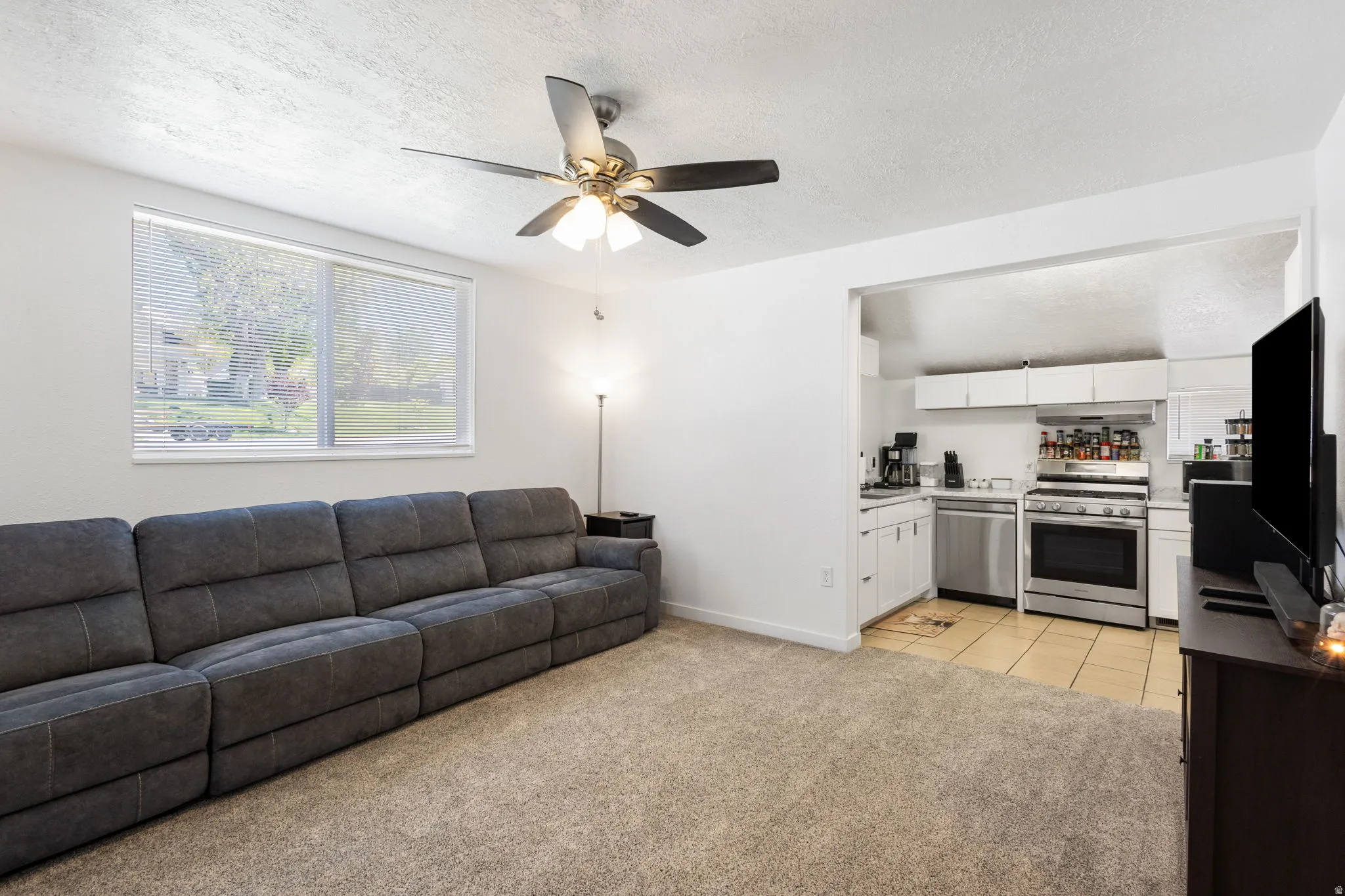 Living room with light colored carpet, a textured ceiling, a ceiling fan, and light tile patterned floors