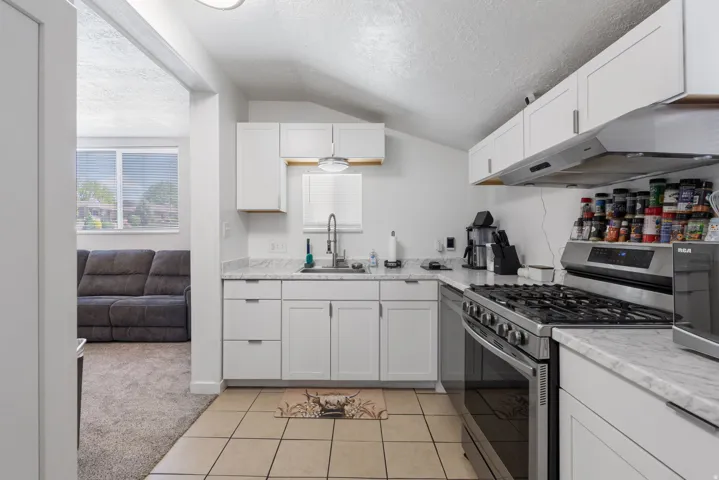 Kitchen featuring stainless steel range with gas cooktop, white cabinets, light colored carpet, light tile patterned flooring, and light stone counters