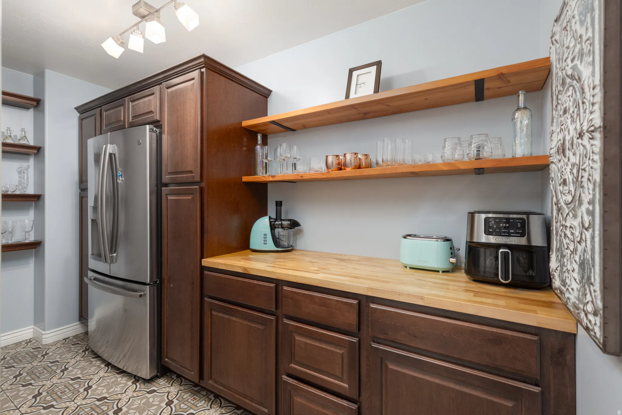 Butler's pantry-  featuring open shelves, wood counters, dark wood finish cabinetry, stainless steel fridge with ice dispenser, and light tile patterned floors