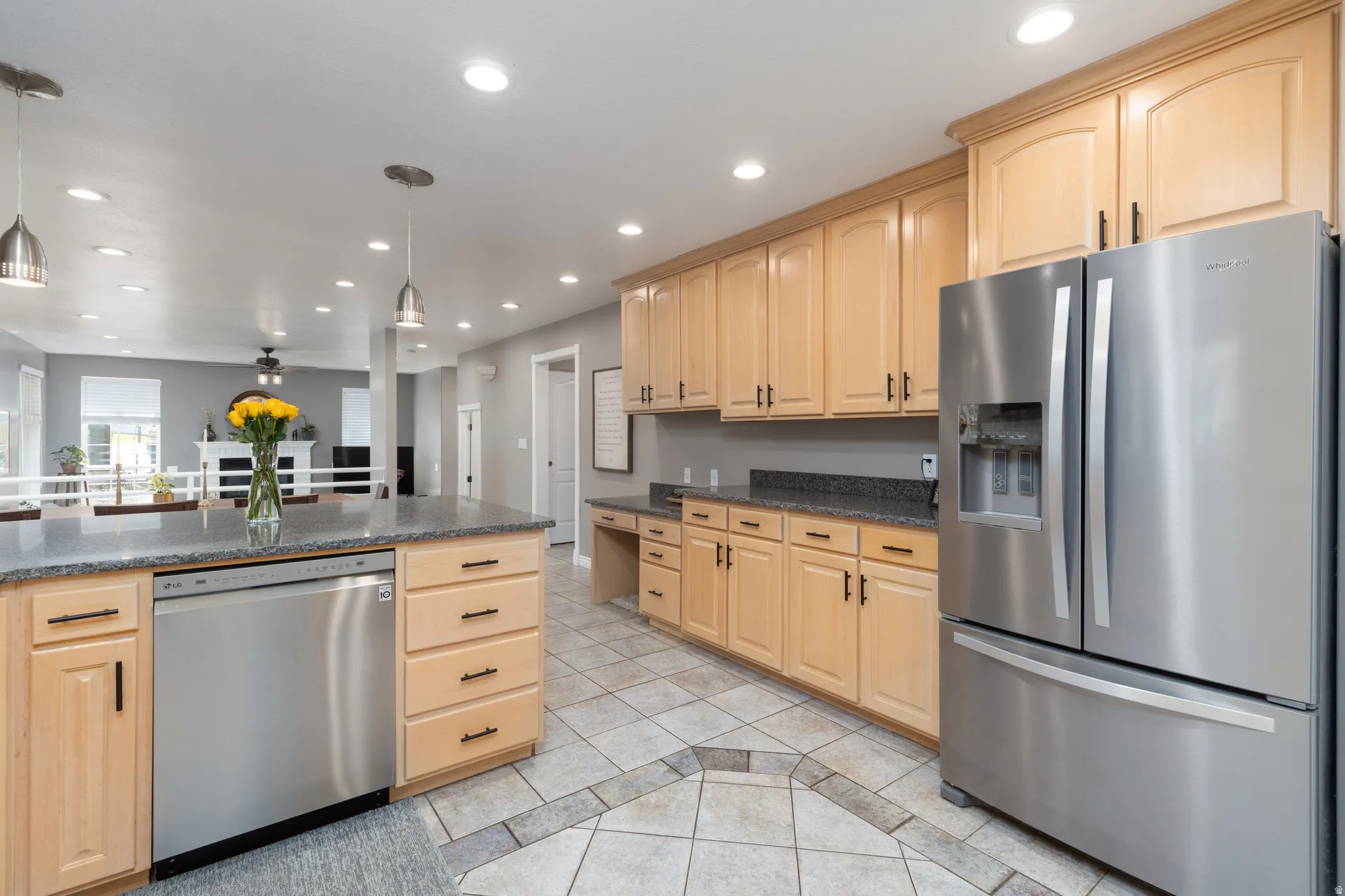Kitchen with stainless steel appliances, light wood finish cabinets, light tile patterned flooring, decorative light fixtures, and dark stone countertops