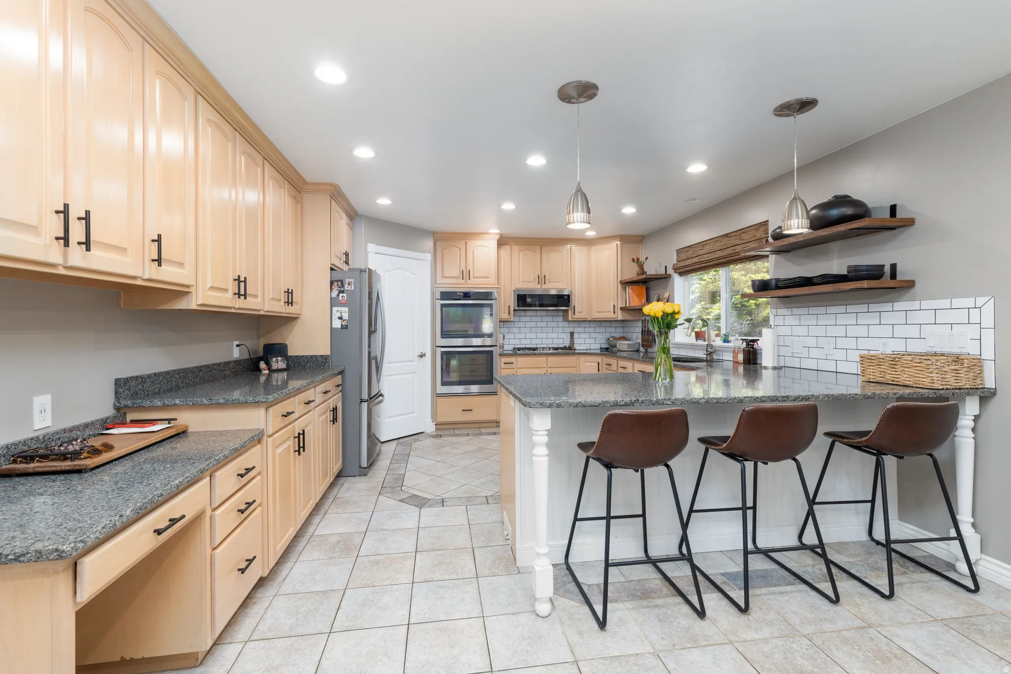 Kitchen featuring open shelves, a peninsula, light wood finish cabinetry, stainless steel appliances, and decorative light fixtures