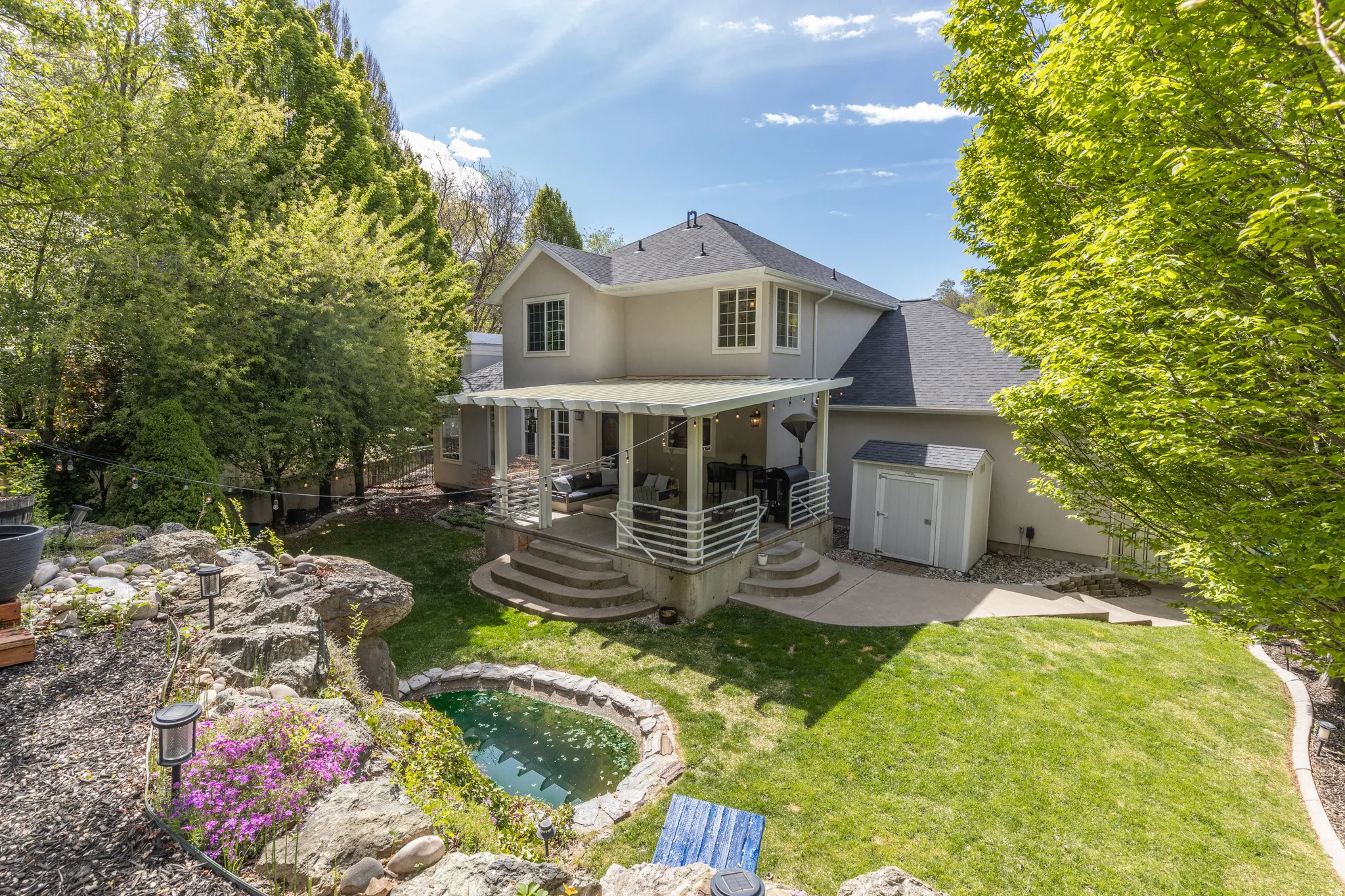 Back of property featuring a jacuzzi, a shingled roof, stucco siding, a garden pond, and a lawn