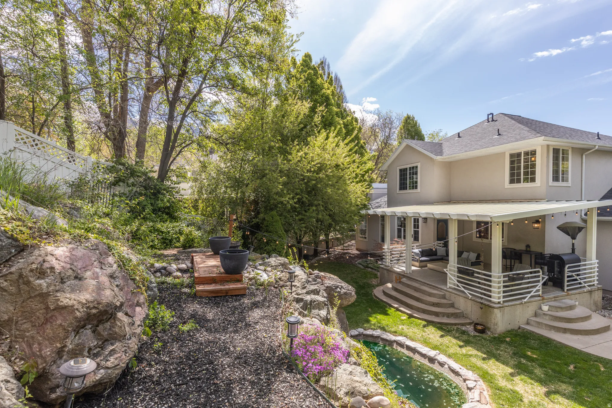 Back of house featuring a wooden deck, a garden pond, stucco siding, and roof with shingles