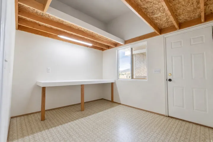 Open-concept room featuring exposed wooden ceiling beams and a built-in white desk