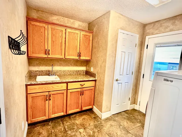 Utility area featuring wood cabinetry, a built-in sink with a chrome faucet, a stone-finish countertop, and tile flooring