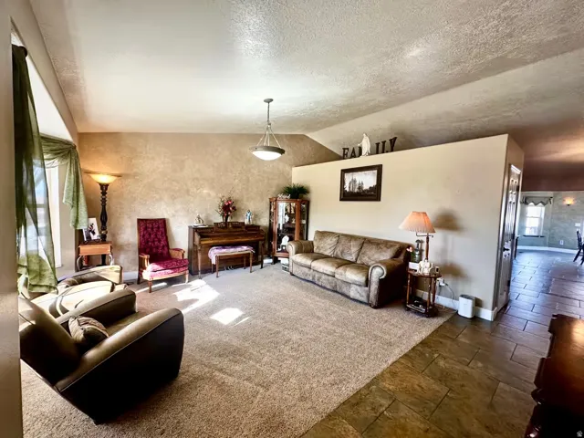 Spacious living area featuring textured wall finish, a sloped ceiling, recessed wall alcove, and a combination of neutral carpet and stone-finish tile flooring