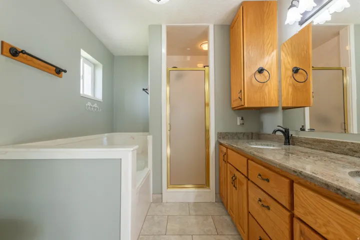 Full bath featuring double vanity, a bath, a stall shower, light tile patterned floors, and a textured ceiling