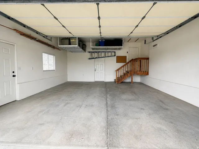Spacious garage featuring a concrete floor, overhead storage racks, a window, and a wood staircase