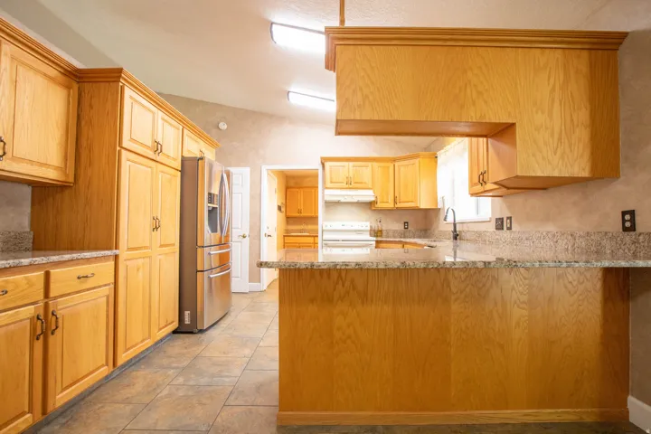 Kitchen with light stone counters, lofted ceiling, stainless steel fridge, a peninsula, and white electric stove