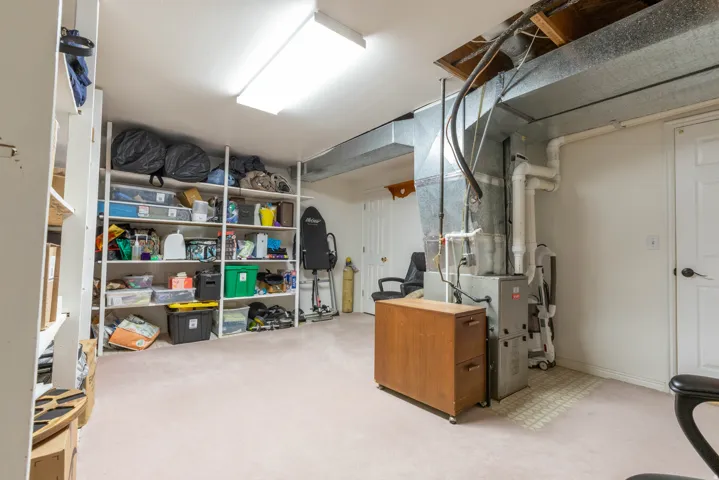 Unfinished below grade area featuring heating unit and light colored carpet