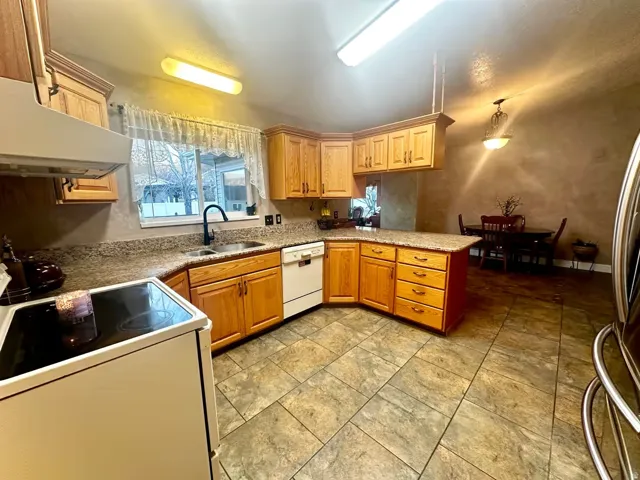 Kitchen featuring a corner sink, wood cabinetry, stone-look countertops, tiled flooring, and a dining area