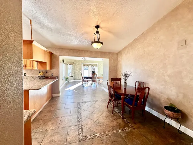 Open-concept interior featuring light wood cabinetry, stone-finish countertops, and ceramic tile flooring with decorative mosaic inlay