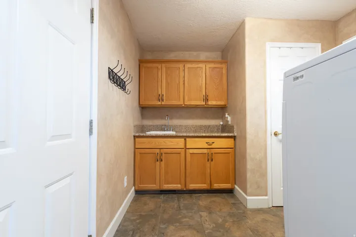 Bar area with washer / clothes dryer, light stone countertops, wood finish cabinets, and a textured ceiling
