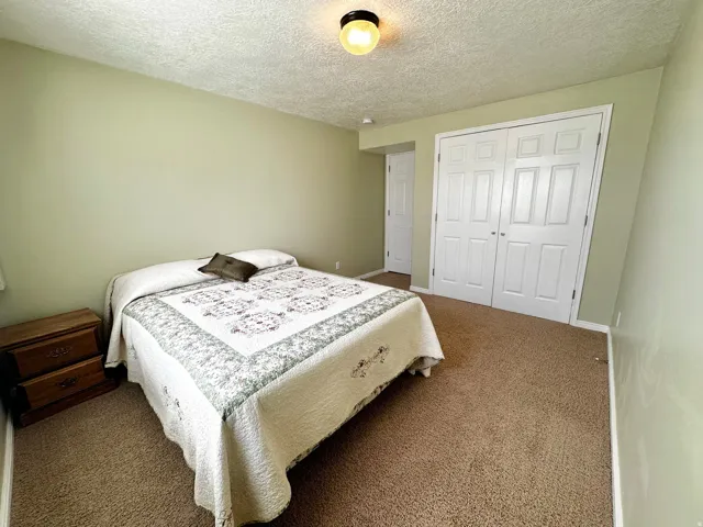 Bedroom featuring textured ceilings, light green walls, brown carpeting, and white bi-fold closet doors