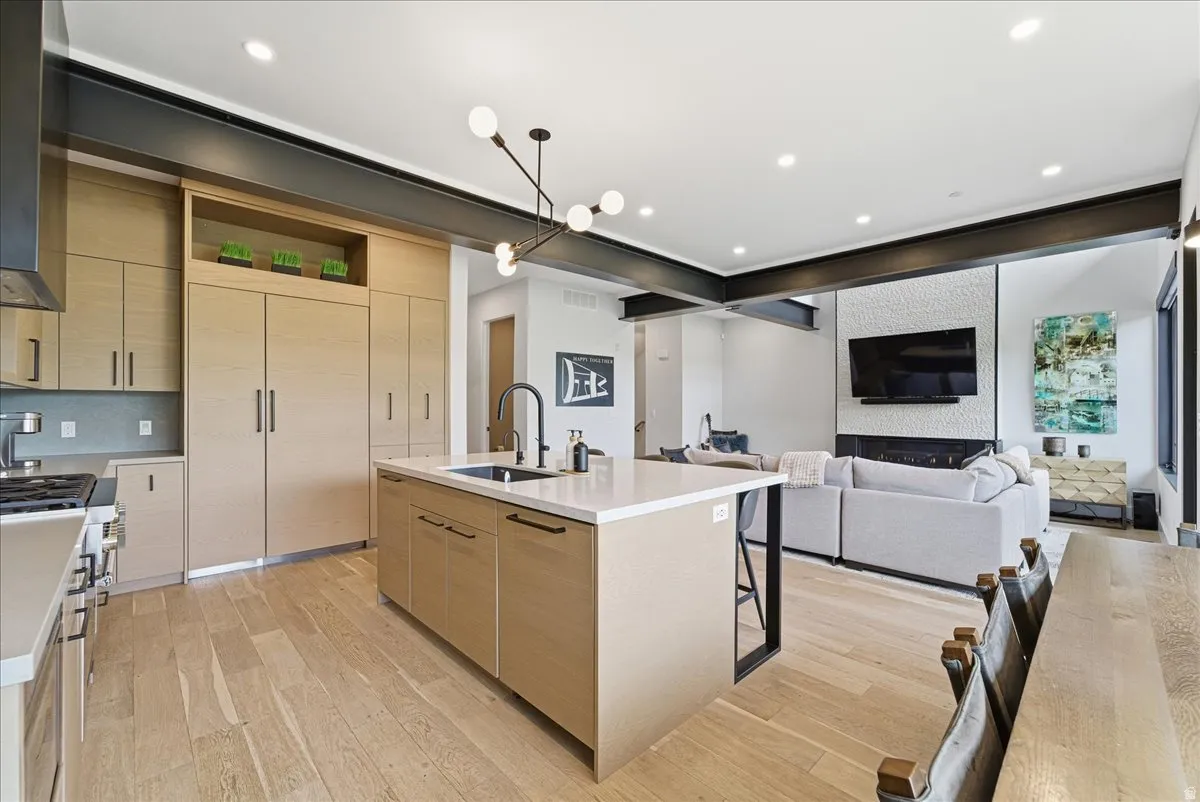 Kitchen with light wood finish cabinets, a kitchen island with sink, open shelves, and light wood-type flooring
