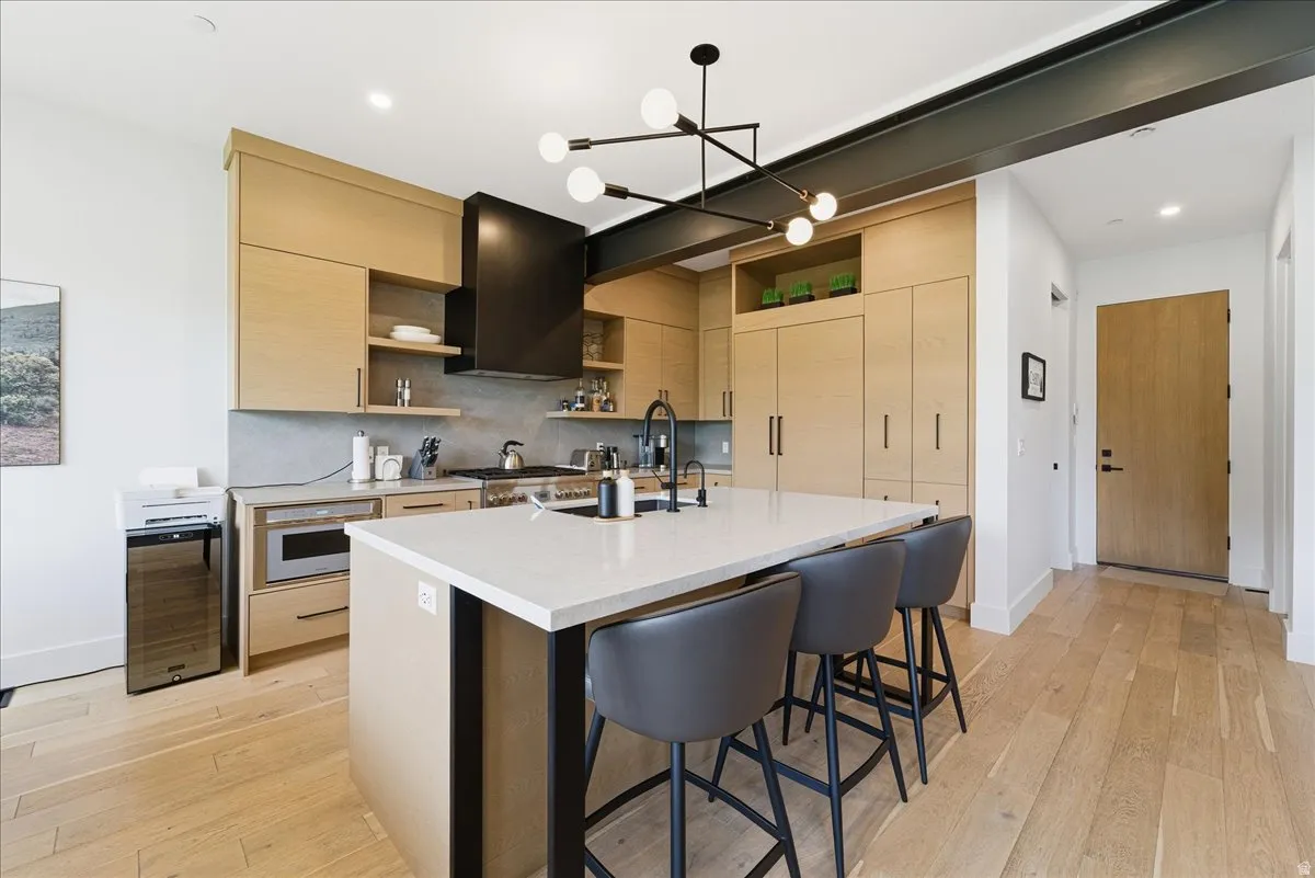 Kitchen featuring open shelves, light wood finish cabinets, a kitchen breakfast bar, a center island with sink, and a chandelier