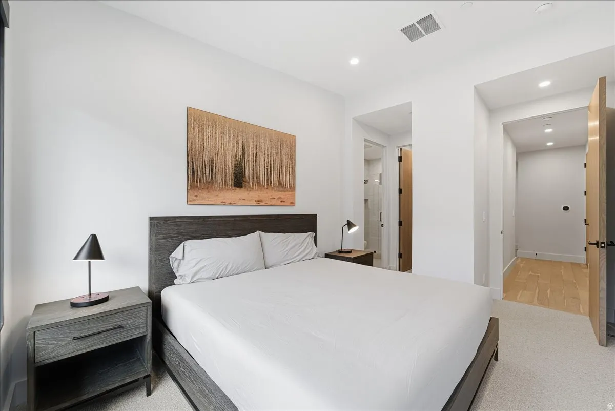 Bedroom with ensuite bathroom, light carpet, and recessed lighting