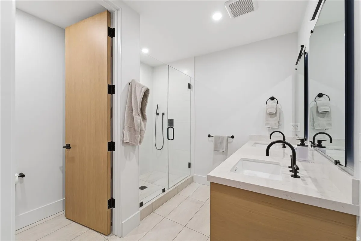 Full bathroom with a shower stall, double vanity, recessed lighting, and light tile patterned floors