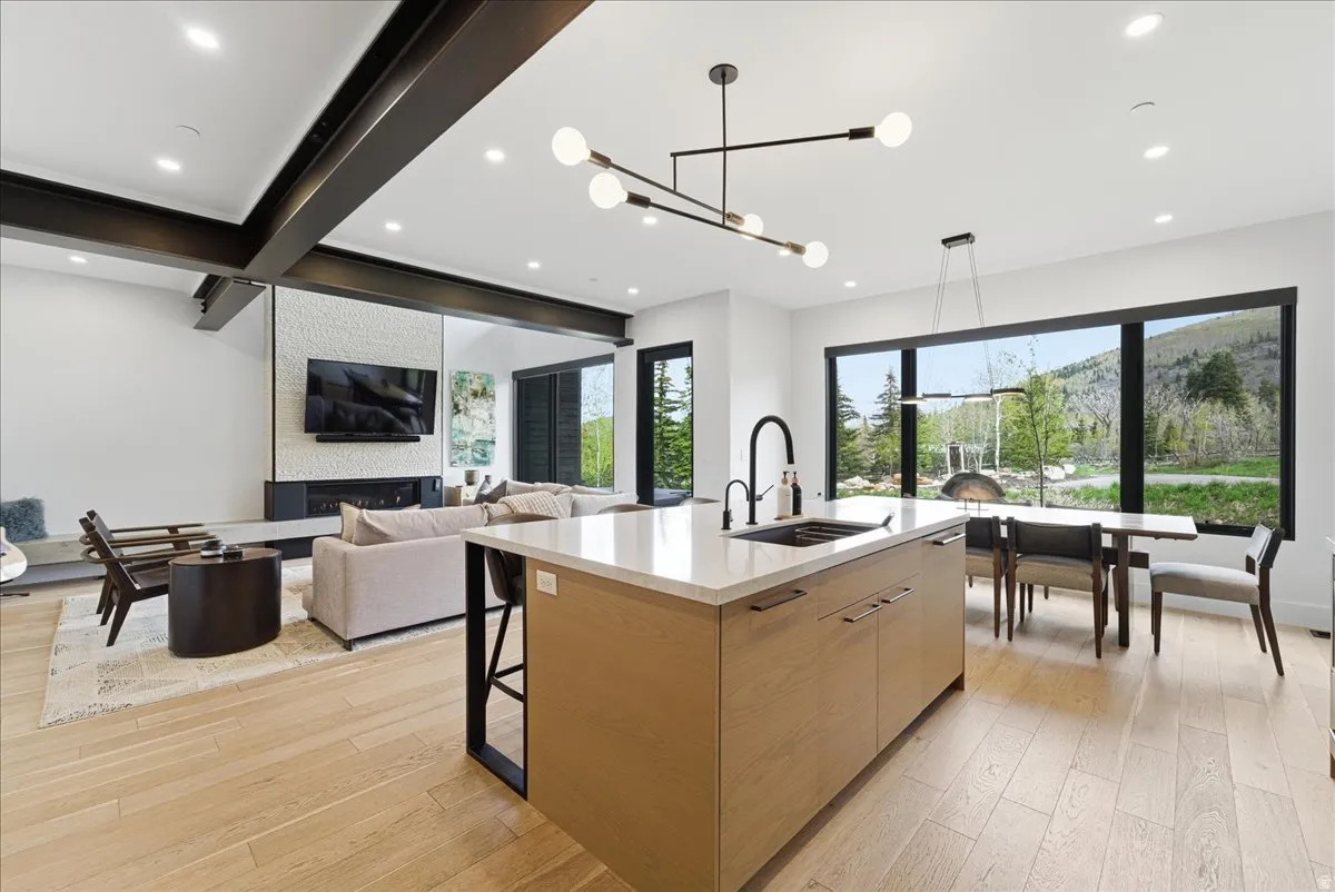 Kitchen featuring modern cabinets, a kitchen island with sink, light stone counters, light wood-type flooring, and beam ceiling