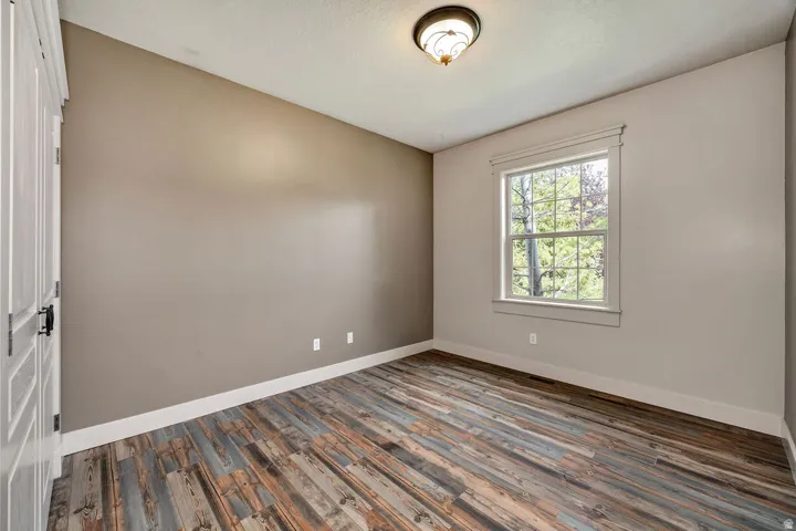 Room featuring wood-finish flooring, a single window with detailed trim, and a semi-flush mount ceiling light