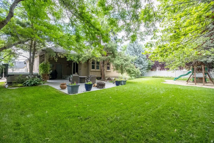 Spacious backyard featuring a manicured lawn, established trees, and a hardscaped patio with outdoor seating