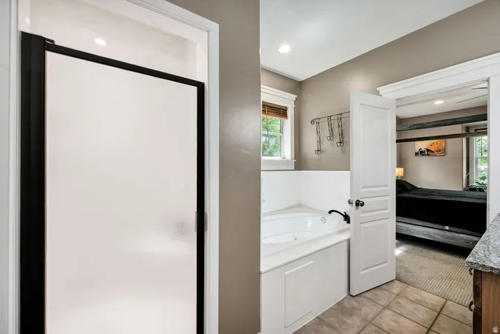 Frosted glass shower enclosure with black trim, corner jetted tub, tile flooring, and a window with blinds