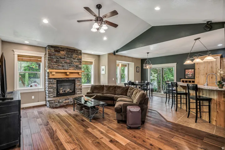 Stone-clad fireplace with wood mantle, vaulted ceilings, recessed lighting, and wood-finish flooring