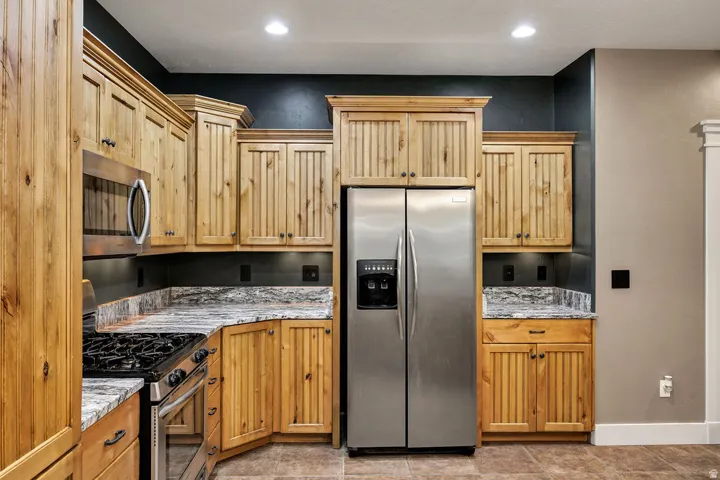 Kitchen featuring natural wood cabinetry with crown molding, stainless steel appliances, granite countertops, and recessed lighting