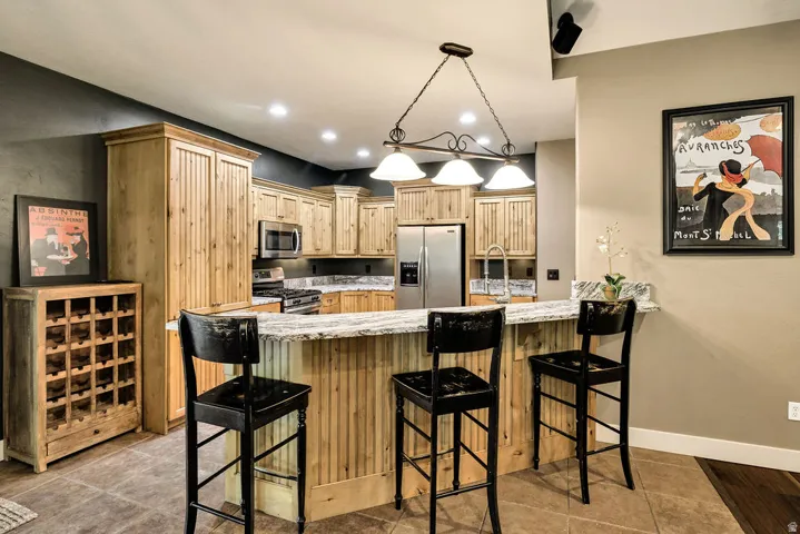 Kitchen featuring natural wood cabinetry, stainless steel appliances, granite countertops, and a peninsula with a breakfast bar