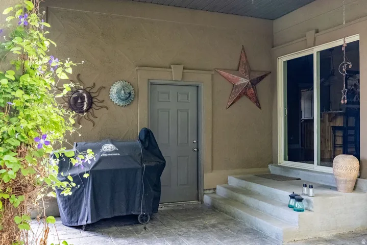 Covered patio area featuring a textured stucco exterior, a gray paneled door, and concrete steps