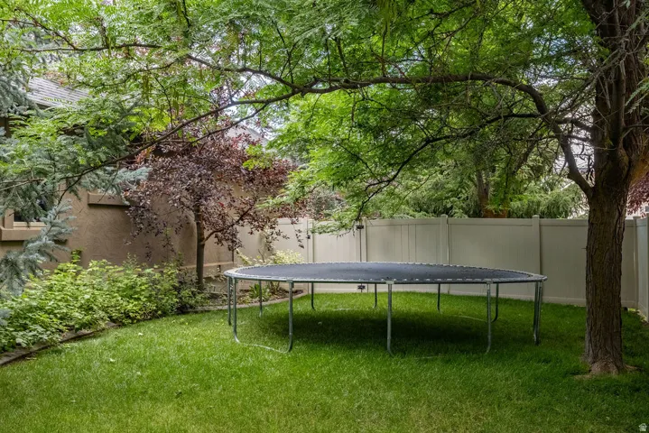 Spacious backyard featuring a lush green lawn, mature trees providing natural shade, and a privacy fence