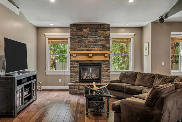Living area featuring a stone-clad fireplace with a wood mantel, wood-finish flooring, recessed lighting, and multiple windows with white trim