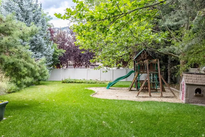Expansive backyard featuring a lush lawn, mature trees, and a white privacy fence